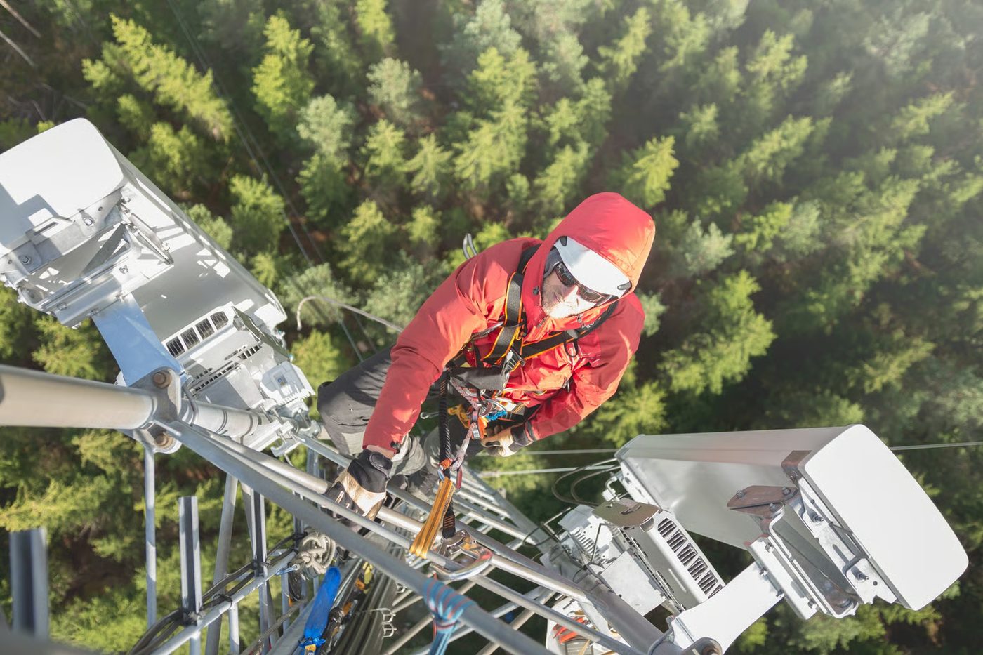 Tower climber on a wireless tower performing equipment work above a forest.